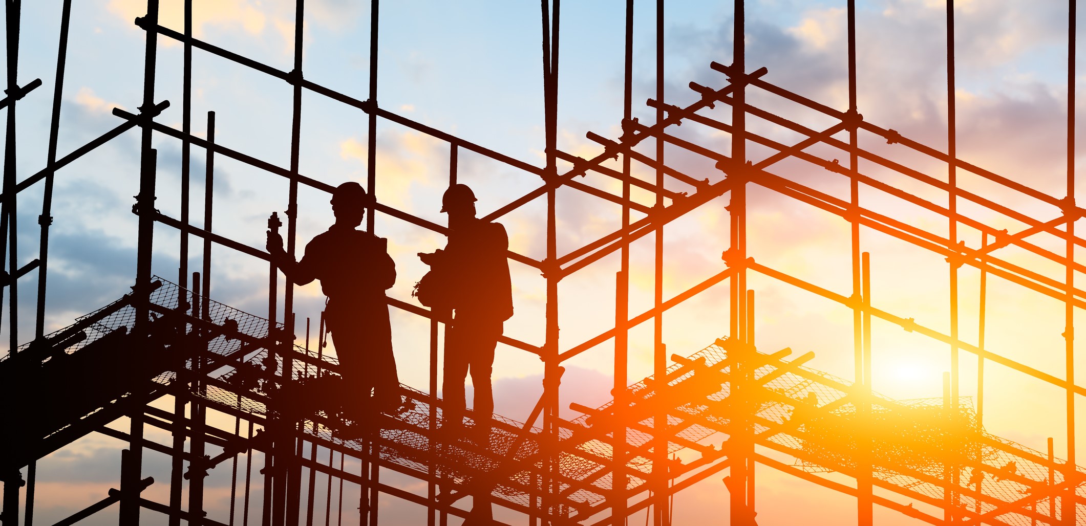 Silhouettes of two construction workers standing on scaffolding at sunset 