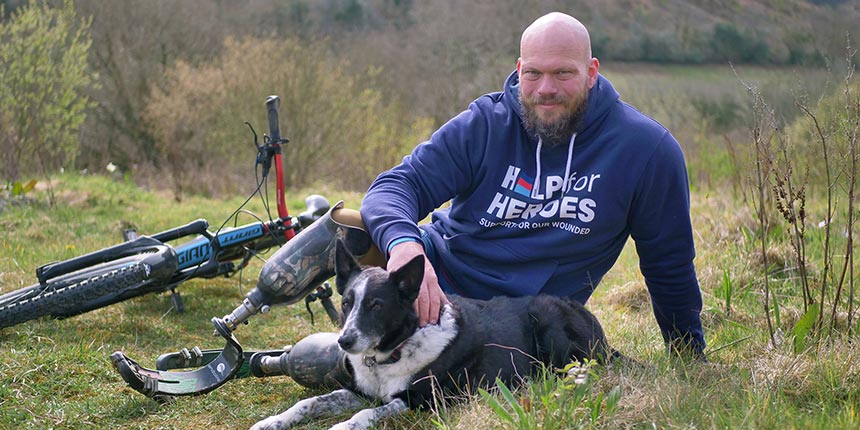 Former soldier Bruce - a double amputee, and one of many veterans supported by Help for Heroes sat with his dog and mountain bike sat in countryside