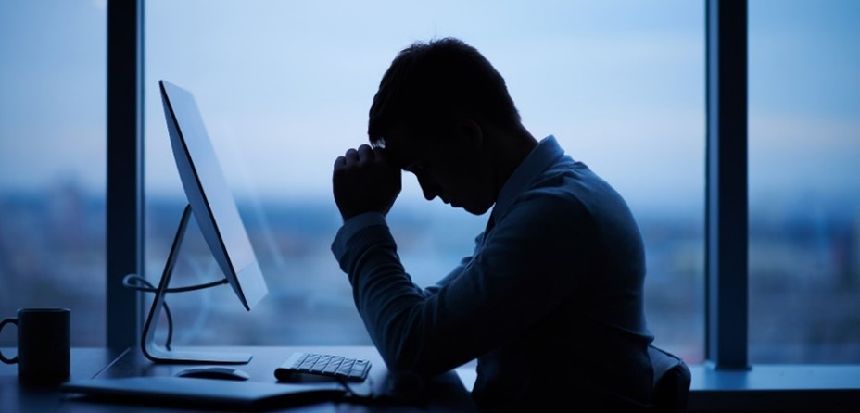 Image of man with head in hand in front of a laptop