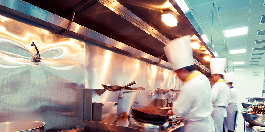 Chefs cooking over a hob in a narrow commercial kitchen. 