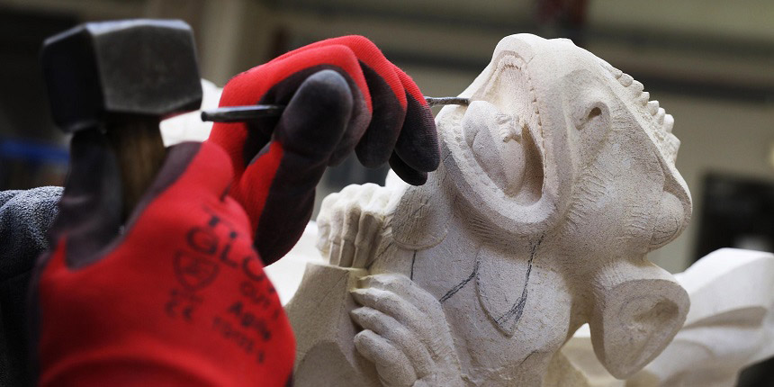 Close up of a pair of hands chiseling a stone gargoyle